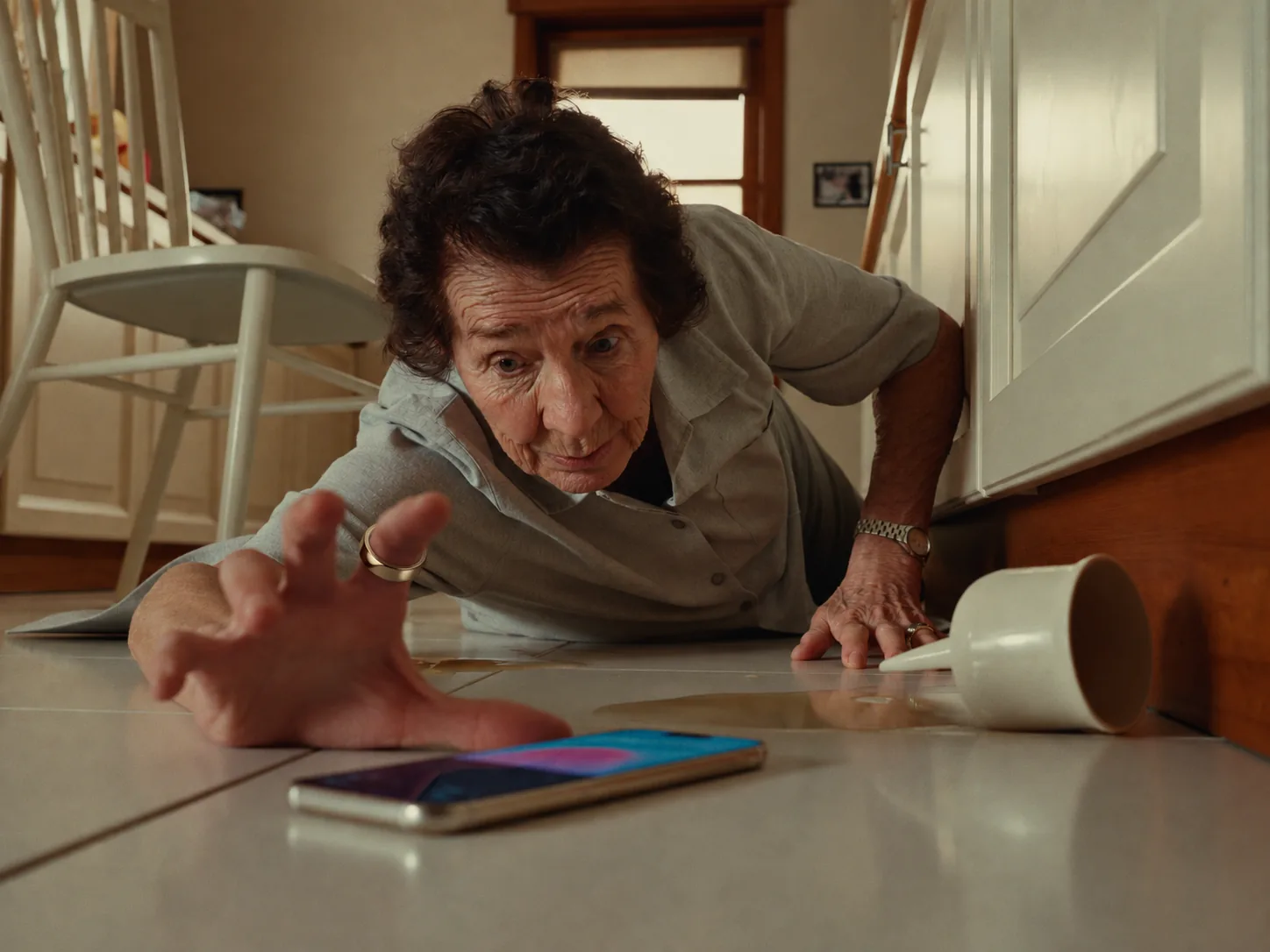 An older woman wearing a HOPE ring reaches for her phone after a fall in the kitchen