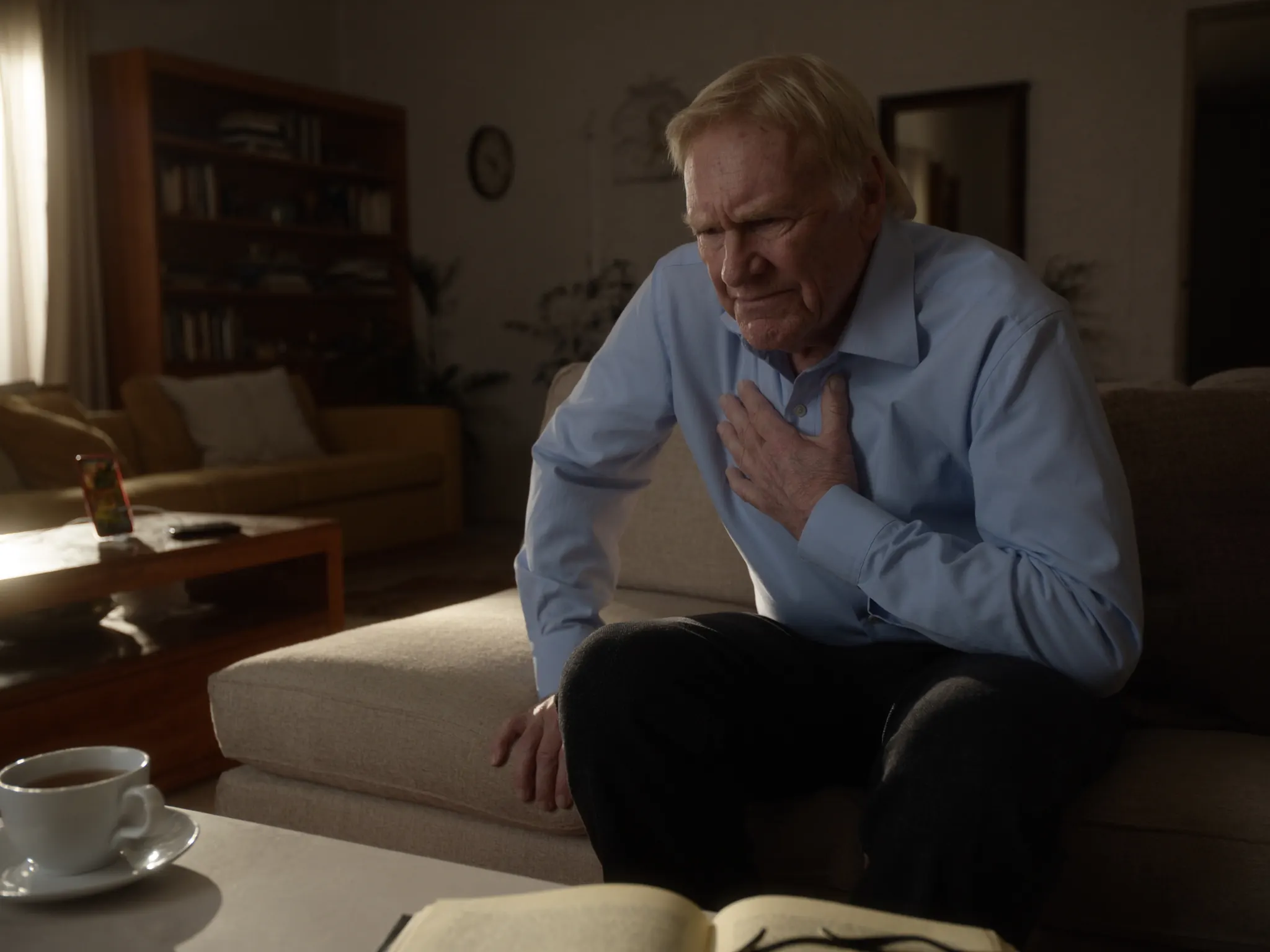 An older man on his couch holds his chest