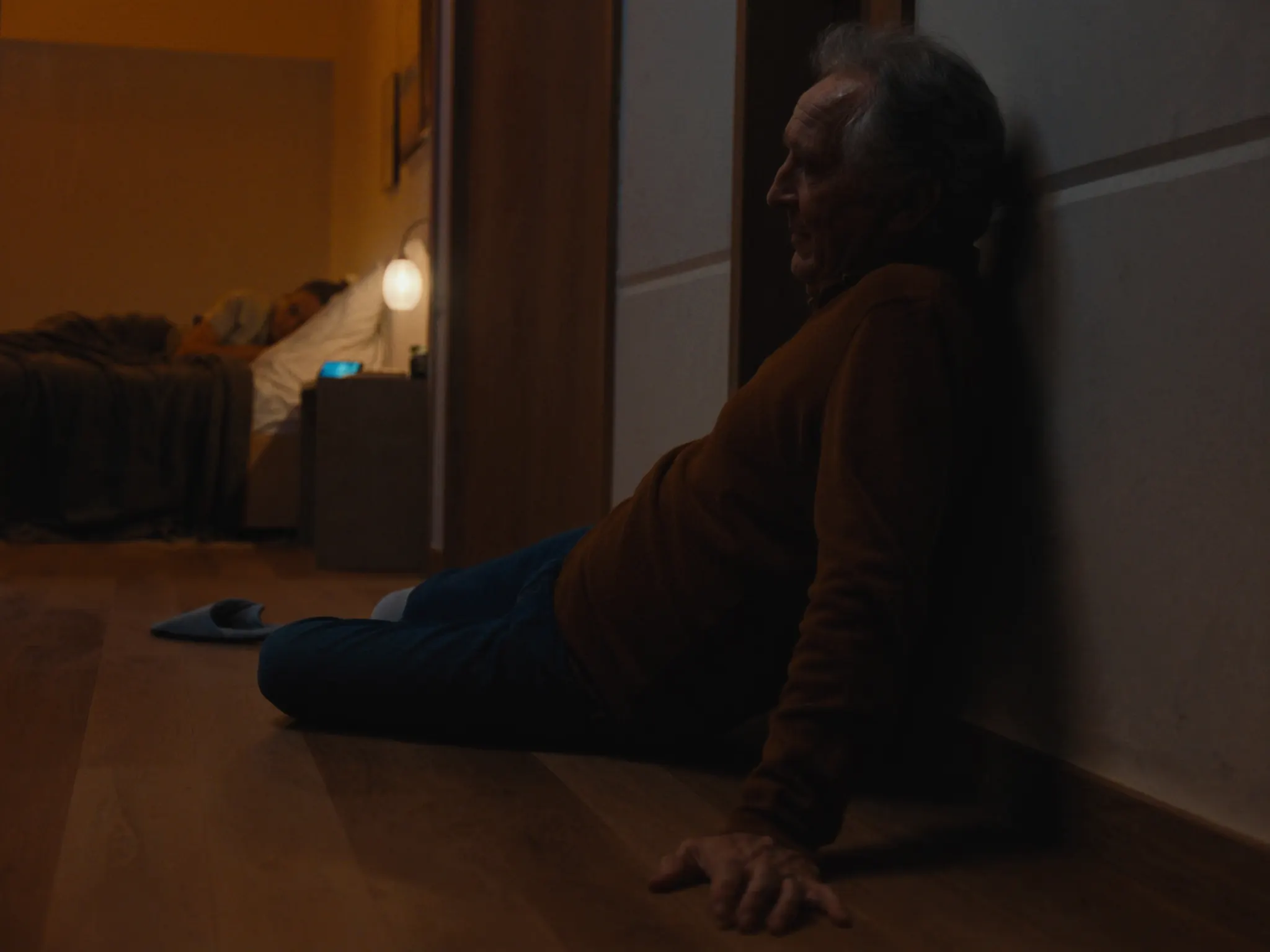 An older man sits on the floor of a dark hallway after a fall