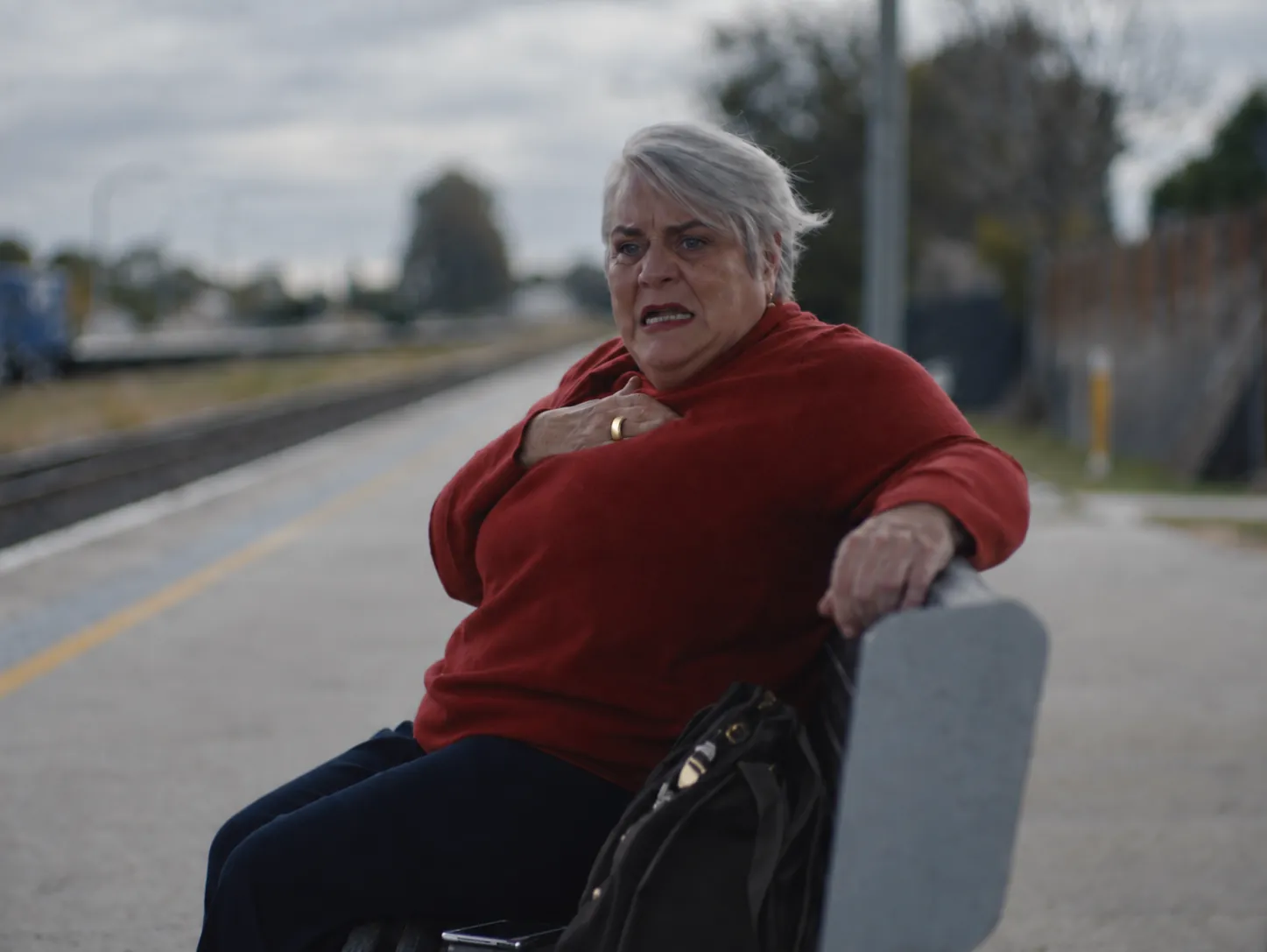 An older woman at a train station holds her chest